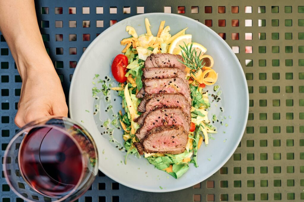 Plate with sliced steak and salad, shot from above with a glass of wine